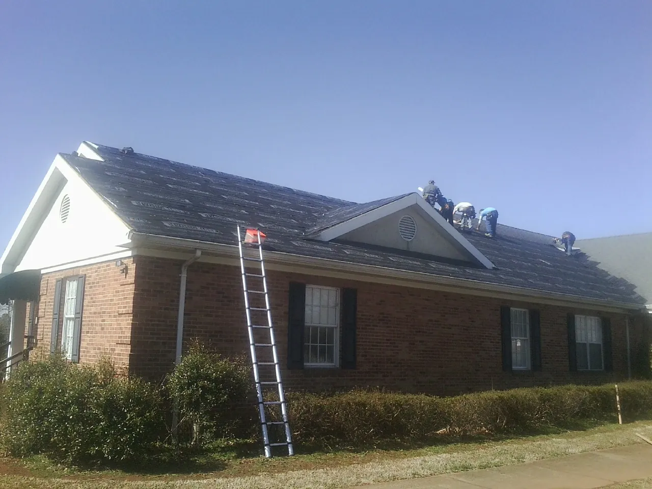 Crew tearing shingles off a brick ranch roof with a ladder set — Emergency Roof Repair work by our crew in Keyes