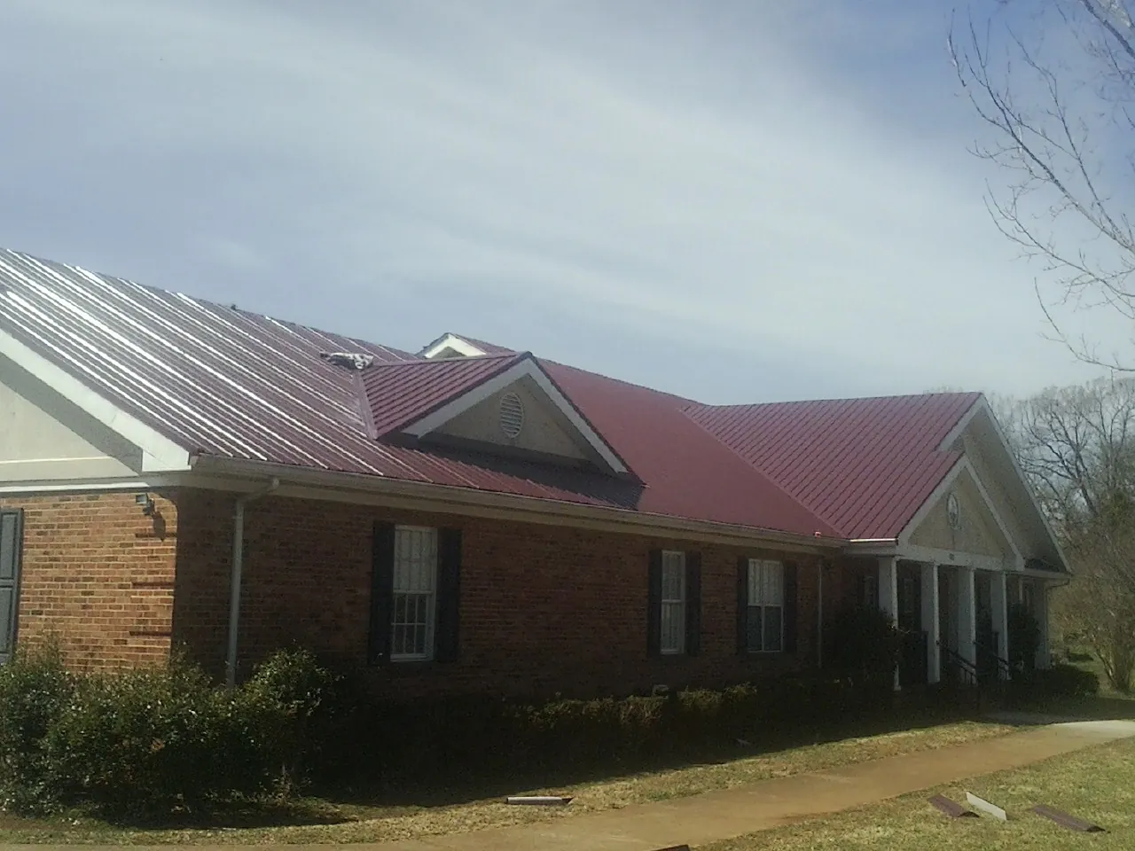 Red metal roof with gabled entries on a long brick building, from a Hail Damage Roof Repair job in Keyes