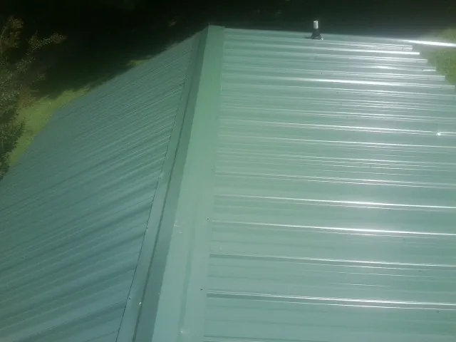 New green metal panels meeting at the ridge of a roof — Flat Roof Repair work by our crew in Keyes