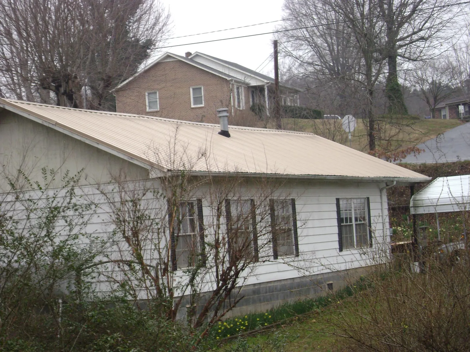 Tan metal roof on a white sided house set into a hillside — Commercial Roofing by Roofing Brothers in Keyes