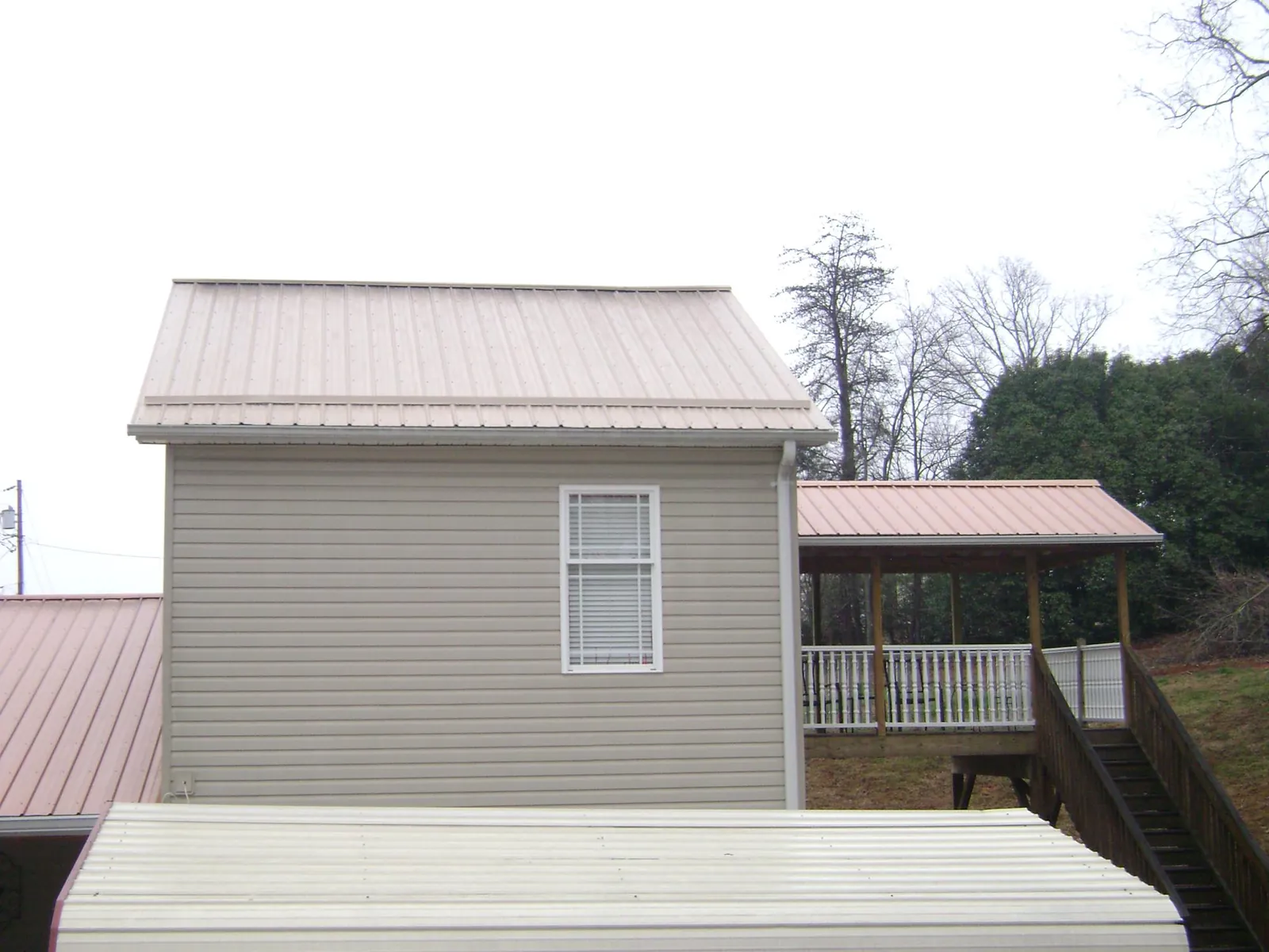 Tan metal roofs on a two story addition and attached porch, from a Roof Replacement job in Keyes